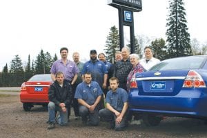 Staff photo/Rhonda Silence The Lashinski family and their employees hope to continue to serve the community as a GM/Chevrolet dealership in Grand Marais. (L-R, front) Sam Bly, Dave Schulberg, Gideon Silence. (L-R, standing) Steve Lashinski, Jason Lashinski, Joe Thompson, Tom Byholm, Daniel Lashinski, Gene and Karen Lashinski, Jarid Lashinski. (Not pictured: Sherry Lashinski, Jamin Lashinski.)