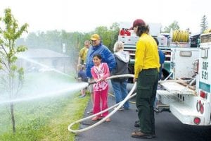 Top: Isabella Marsden and her dad, Steve Marsden, of Lakeville, MN, were among the many Centennial visitors who checked out the firefighting equipment, taking a turn on the hose. Above: Wilderness Ranger Betsy Kurtz oversaw a logsawing demonstration. Luke Johnson and Claire LaVigne from the Cooperation Station Explorer's Club took a turn on the saw.