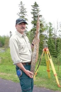 Forest Service surveyor Harvey Sobieck offered glimpses through the surveyor's lens—and the chance to touch a piece of history. The aged wood he is holding is a bearing tree marker from a survey done off the Greenwood Road sometime in the 1880s. The stamp on the old jack pine denoted 