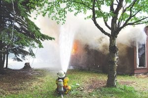 The Grand Marais Volunteer Fire Department conducted a live structure burn with instructors from Mesabi Range Community & Technical College on Saturday, July 11. Top: Grand Marais Fire Chief Ben Silence practices hose techniques. Left: Firefighters fought the fire inside and out, working in teams.