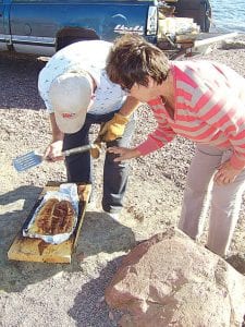 Left: Gene Erickson and Carol Backlund check to see if the salmon is done after it was cooked standing on end in the fire pit in Harbor Park Saturday, July 11, 2009.