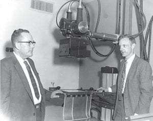 Above, Dr. W. R. Smith on left, and Dr. Richard Soderberg, point out expensive equipment in the X-ray room. Price tag was $13,500.00