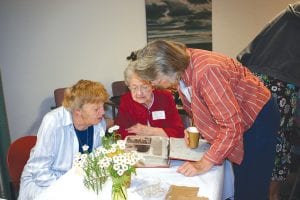 Staff photos/Rhonda Silence Vi Wonser, Phyllis Noyes, and Sharon Eliasen take a stroll down memory lane with the North Shore Hospital Auxiliary scrapbook during the Hospital’s 50th Anniversary celebration.