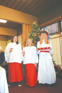 Above: In Scandinavian tradition, St. Lucia is the “queen of lights” bringing the promise of longer days. On the darkest day in the Swedish winter, normally December 13, it is considered bad luck to eat after dawn, so the children of the home treat parents to a special breakfast in bed, with the oldest girl portraying St. Lucia. St. Lucia wears a white dress and a crown of pine boughs. On the crown are seven candles, to represent the coming of brighter days. Around her waist she wears a bright red sash. St. Lucia Jessica Berg-Collman, daughter of Julie Collman and Mike Berg, is attended by Anika Schwarz, daughter of David and Beth Schwarz (far left) and Taryn Hansen, daughter of Teresa and the late Jeff Hansen. Upper right: Along with wonderful welcoming piano music by Mike Chmelik and a lovely piano-flute duet by Mildred Thoreson and Philis Anderson, cellist Alex and violinist Daniel Ditmanson offered some beautiful Christmas carols. Above right: Barb Erickson and Irene Malner put some finishing touches on the Christmas tree at Julefest. Barb has faithfully decorated the tree for 35 Julefest celebrations.