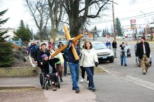 Armed with umbrellas under threatening skies, about 40 people came out for the Annual Community Cross Walk on Good Friday, April 2. The faithful followed the cross from the Evangelical Free Church, through Grand Marais and back to St. John’s Catholic Church where an ecumenical Good Friday Service was held. The groups paused at each church and at symbolic points on the east and west ends of Grand Marais to pray for churches in and out of Grand Marais. The rain held off during the walk during which community members took turns bearing the cross. Pictured above, Paul Muus takes a turn carrying the wooden cross, assisted by Nicki Boostrom and Daniel Ditmanson.