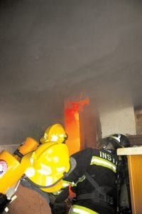 Ready to go. Firefighters from area fire departments participated in live burn training at a house in Grand Marais on Saturday, April 10. Left: Team 2 (Cory Ronden, Kim Dunsmoor and Linda Bloomquist) is geared up and ready to enter the burning building. Above: Inside the burning structure, firefighter trainee team 1 (Shane Danielson, Jacob Wilson, Paul Olin) prepare to enter a burning room.