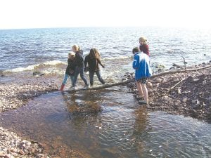 Girl Scouts gathered at the mouth of the Kadunce River east of Grand Marais on May 6, 2010. During their outing they learned about erosion and helped pick up trash. Girl Scouts help one another across a log at the mouth of the river.