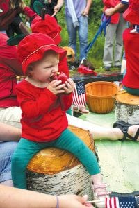 Left: On a float “As American As Apple Pie,” apple-capped parade participants tossed apple fruit bars, cups of applesauce, and real apples—except for this little girl who decided to have a snack. Right: Katrina Evans of St. Paul checks out the fish-shaped potholders created by Iola Wotisciak of Grand Marais. Iola donates 100% of the money made on her unique potholders to the Birch Grove Community School lunch program. Before the 4th of July celebration, Iola had already raised $500 for the school.