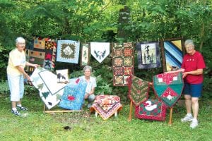 The Mid-Trail Benefit for the Gunflint Trail Volunteer Fire Department is renowned for its lovely handcrafted quilts. Pictured here with items that will be available at the August 14 event is (L-R) Ina Huggenvik, Sue Sutphin and Keitha Herron. Mid-Trail auction and more