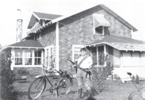 This is a photo of Clarence Thompson in front of his childhood home, the Thompson homestead. Born in 1927, Clarence was the youngest of five boys and one girl. The home was originally near Thompson Lake but was eventually moved to Two Island Lake, where it still stands.