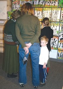 Tighe McHugh standing by his mother, Carrie McHugh. Tighe’s sister Maya is in front of them, checking out the wall covered with interesting birch tree paintings.