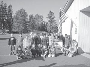 Third graders at Sawtooth Mountain Elementary observed the democratic voting process on November 2, 2010. Above: Posing for a photo outside the polls (left to right, front) Garret Schlienz, Shaelynn Novitsky, Abbie Crawford, Lucy Shaw, Emma Gesch, Bianca Zimmer, Paige Everson, Mallory Goettl. Left to right, back) Chase Gwash, Mason Liljestrand, A. J. Owens, Trent Spry, Alyssa Spry, Jaymie Kirk, Zach Stirewalt, Adam Dorr, Sam Sietsema, Pete Sutton, Dominic Wilson, Haley Richardson, Jessup Schlienz, Ian Waltz, Ryan Cox. Left: Dominic Wilson looking at the camera while Election Judge Nelda Westerlind explains the ballot. Students were then able to watch the voting process as some school staff members voted.