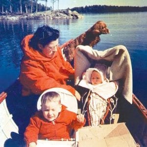 Old photos brought back happy memories of Dinna and the Madsen family at the lake. This photo is of “Dinna, Chris, Sandy, and Fritzy.” Note the Tikinagan that Jack Powell helped her make. Jack and Dinna cut down a cedar tree, and from the tree they made the backboard noting that the head of the board would remain in the same direction in which the tree was growing upward. From an ash tree they made the bow, which served as a roll bar and also a frame to support mosquito netting or a blanket in which to shade the baby's face.