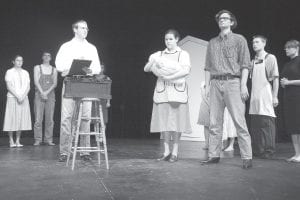 Townspeople tensely await the outcome of the “lottery” held each June 27 in their village. Joe Summers (Jesse Johnson), center with clipboard, oversees the drawing. Bill Hutchinson ( Will Brandenberg) holds the ticket that determines the fate of his wife, Tessie (Sarah Larsen), who clutches their baby, Davey.