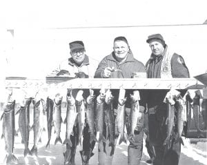 With another Trout Derby coming up on March 13, this one sponsored by the Cook County Ridge Riders Snowmobile Club, we thought it would be fun to share another trout derby photo. Julie Carlson of Joynes Department Store has discovered a treasure trove of Lions Club Trout Derby photos at the Grand Marais store. The photos were taken by M.J. Humphrey. According to the note on the back of the photo, not all of the fellows checking in the catch are known. They were Bob Fry, an unknown man smoking a pipe, and Bernie Larsen. The lake where this trout derby took place is also unknown. Does anyone know?