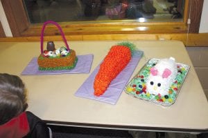 Above left: There was a wonderful assortment of cakes on the silent auction, donated by supporters of KidsPlus. The winners were (L-R) the Easter basket and the Carrot Cake by Courtney and Shauna Blake and the Funfetti Bunny Cake (complete with a marshmallow tail!) by Virginia Palmer. The real winners were the folks who got to take them home! Above: Kevin and Kylie Viren were very successful in finding the eggs that were half buried in the snow. Kevin Viren found one “really big!” egg. Left: Piper and Maya Denewith didn’t mind the snow at all as they filled their Easter baskets.