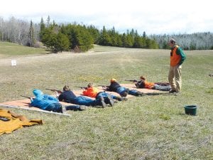 Paul Eiler supervises students firing .22 rifles from prone position at targets 50 feet distant.