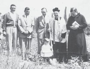 St. John’s Catholic Church in Grand Marais celebrates several significant anniversaries this Saturday, June 25, so we thought it would be fun to share a photo from the church’s archives of the groundbreaking of the current church building at 10 East Fifth Street. Pictured here at the groundbreaking were (L-R) Wes Backlund, Rudy Backlund, Hugh Ridgeway, Father Candrian, Brother Elmer Cicci and the cute little girl lending a hand is Carline Sjoberg.