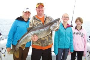 On Sunday, June 26, the young ladies on the right, Emily Grote and her friend Katie from Eden Prairie, reeled in this monster lake trout. For 15 minutes they took turns with one holding the rod while the other reeled, switching off when they got tired. Dave Grote stepped in as the fish neared the boat and the girls tired, to slide the 26-pound, 44 inch-long fish into the landing net. Mom Katie Grote was also on hand to watch the action. It was released to be caught again.