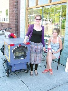 Nora Richards (left) is staying in good shape biking around town helping others refuel with goodies from Lola’s Sweet Life Bakery of Grand Marais. She is the friendliest (well, maybe the only, but even if she weren’t the only she would still be the friendliest) biking peddler in town, selling things like scones and cookies and empanadas. Nora’s friend and customer Stefanie Mitchell, manager of Threads, is enjoying one of the delectable delicacies.