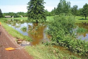 Although the flooding in downtown Grand Marais drew a lot of attention, there was water damage throughout the county. Above: Gunflint Hills Golf Course gained an additional water hole on the course because of the flooded ditch. Right: The 3.5 to 3.75-inches of rain that fell overnight on July 20 caused damage to a lot of roads like Linnell Road. Far right: Solveig Vick was another Stone Harbor Wilderness Supply staffer who helped ferry customers and merchandise across the flooded city parking lot.