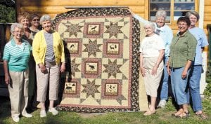 The Mid-Trail Quilters with the beautiful quilt they created for the Mid-Trail Fire Department Fundraiser. The “Among the Stars” quilt features moose, bear, wolf, birds, and deer surrounded by stars. (L-R) Ginny Tuttle, Joan Perusse, Bert Forss, Lee Zopff, Ina Huggenvik, Keitha Herron, Janet Little and Linda Graham. Other quilters not pictured were Sue Sutphin, Judy Edlund, Vonie Swenson, Eleanor Lease, Carol Stockman and Phyllis Olson.