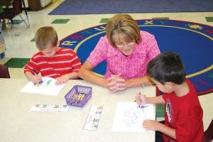 Marshall O'Phelan colors diligently while Jenny Hennessy helps Noah England with his art project. The boys were in the first five minutes of starting their school careers and already hard at work. Their kindergarten teacher, Dena Schliep, had all of the students working on coloring projects within minutes of entering the classroom on the first day of school.