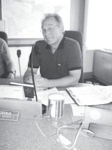 Commissioner Fritz Sobanja at his desk in the Commissioners’ Room at the Cook County Courthouse. He has a sample of a desk lamp in front of him, but it is not plugged in because he does not intend to use the new lamp that will soon sit there at county board meetings. Nine new LED desk lamps are being ordered after the board agreed to stop using the overhead compact fluorescent lights because Commissioner Sobanja has severe negative reactions to them. He has provided the board with information regarding research into the health ramifications of electronic devices and certain types of lighting.