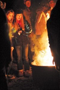 Left: People tossed their “gloomies” on the fire to say a symbolic goodbye to troubling thoughts. Above: Families dressed warm and huddled together to watch the simple, but delightful, puppet show created by Good Harbor Hill Players with lights and shadow.