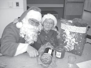 The North Shore Care Center was especially festive for the holidays. The annual Christmas Eve party at North Shore Care Center for residents and families was hosted by Santa (Darrell Smith) and Mrs. Claus (Eleanor Matsis). Above: Santa gives Joyce Kehoe a hug after she opened her gift bag full of colorful yarns. Left: Ruth Helmerson admires the handiwork on a Christmas card from Great Expectations students. The students enjoyed visiting with Care Center residents and bringing Christmas cheer with some holiday tunes.