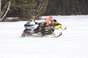 Hungry Jack Lake, in front of Hungry Jack Lodge, was buzzing with exciting activity on Saturday, February 18. Fourteen racers put their sleds on the line for bragging rights and a trophy in the Cook County RidgeRiders Snowmobile Drag Races. A record crowd turned out for the event. Above: Speeding toward the finish line is Colton Deschampe (left lane) and Greg Gresczyk. Left: Race organizers watch a powerful machine takeoff.