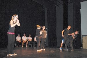 Molly Zafft pretends to be a radio broadcaster informing her listening audience about the antics of her zany cast mates to the right: David Bergstrom threatens to wallop Brad VanDoren while Michaela Buchheit and Lauren Murray look on.