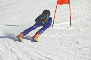 Staying low and riding the edges of his skis, Logan Backstrom, Grand Marais, speeds for another gate in one of the slalom runs he competed in at Steamboat Springs in the Junior Championships held March 15, 16, & 17. Logan placed 35th in the J-4 category out of 80 skiers who qualified from 20 states. To the right, Logan stands smiling while holding up the sign proclaiming the races, which in the past were called the Alpine Junior Olympics. Logan is the son of Rick and Jennifer Backstrom.