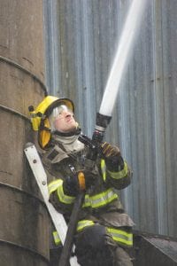 Left: Firefighters used hoses on top and on several areas on the side of the silo to try to extinguish the stubborn burning material inside the silo. Grand Marais firefighter Gideon Silence manned the hose between two of the silos.