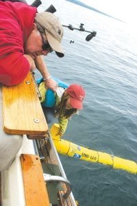 Captain Dave Williams of Fishin’ Chicks Charters grasps UMD grad student Betsy Welsh’s life jacket for safety as she helps lower the Gitchi Gami submersible glider into Lake Superior. Welsh and Assistant Scientist Matt James will stay in contact with the glider as it collects valuable information on Lake Superior.