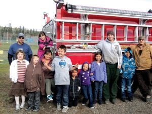 The Grand Portage Fire Department shared the fire safety message with students at Oshki Ogimaag on Thursday, October 11. Right: The firefighters patiently answered many questions about the fire truck. (L-R, front) Alice, Davin, Nashalla, Daunte, Payton, Christina, Niimin, Firefighter Cody Carlson, Jordan, Firefighter Brad Deschampe. (L-R, back) Firefighter Chad Spry, Aurielle (on back of truck). Below: Firefighter Brad Deschampe shows Angel all the levers and buttons used to operate the fire truck.