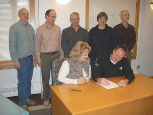 The county board has come to a working agreement with the Duluth Area YMCA for management of the new community center that will be built onto the west wing of the Cook County Schools Complex. Signing the contract is Duluth Area YMCA Executive Director Chris Francis with County Board Chair Jan Hall seated beside him. (Standing, L-R) Commissioner Bruce Martinson, County Auditor-Treasurer Braidy Powers, Commissioner Fritz Sobanja, Commissioner Sue Hakes, and Commissioner Jim Johnson.