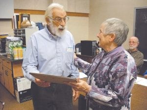 ISD 166 board chair Mary Sanders presents retiring school board member Leonard Sobanja with a plaque announcing the establishment of a new scholarship fund in his honor at a school board meeting December 20. She thanked him for his service to the school district—spanning seven decades—as a teacher, principal, school board member, and champion of the industrial arts program.