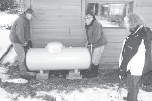 Jess Derscheid, (left), technician for Como Oil and Propane, and Glenn Hellner (center), Hellner Sales and Service, position a propane tank for new customer and REEP client, Carolyn Schmidt (right). The addition of a propane fireplace with other building improvements that include air sealing and insulation will improve the comfort and operating cost of the home.