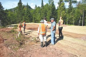 A representative of the Great Lakes Commission that provided a large grant in 2010 for erosion control projects on the Poplar River in Lutsen took a tour of the projects on August 6. Left: A tightline – a pipe underneath the ground – has been installed this summer as part of the Caribou Highlands Flowpath project. Above: Representatives of Cook County Soil & Water and the Poplar River Management Board along with Gary Overmeier of the Great Lakes Commission and engineering consultant Curt Sparks view a specially designed ditch that diffuses the energy of water running beside a narrow maintenance roadway that traverses the hillside. The system includes culverts, collection basins, and rock-lined channels that direct the water and reduce the force of its flow.