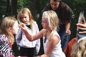 Above left: There were some fun and artistic kids’ crafts. Emma, 5, watches intently as Sylvia paints lovely flowers on Jordan’s face. Above right: Amanda Hand’s lovely voice blended beautifully with her stage mates, Yvonne Mills, Barb LaVigne, accompanied by Russ Viton on guitar.