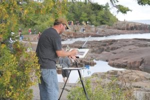 The 11th annual Plein Air Grand Marais event was held September 6 – 29. Seventy artists could be spotted throughout the county painting outdoors. Many art lovers headed to The Point Thursday, September 12 to watch the Quick Paint competition. Top: Tucked into a wooded spot, this painter is part of the scenery. Upper left: This artist meticulously puts the finishing touches on a painting of the walkway to the lighthouse. Upper right: Viewers can get a bird’s eye view of the artists at work. Right: Richard Abraham, winner of the Quick Paint competition, looks at the Hjordis on the horizon. The paintings from Plein Air Grand Marais will be on display at the Grand Marais Art Colony until September 29.