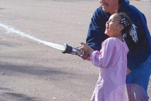 Left: Nevaeh loved using the fire hose at Birch Grove Community School. Above: Lee Jahnke of the Tofte Fire Department shows Sierra how to turn the water on and off.