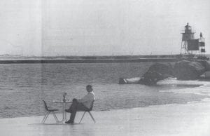 Table for one! Neil Turner of Prior Lake relaxes at a table set on the ice of the Grand Marais harbor near the Angry Trout Café. This photo from the March 21, 1994 News-Herald illustrates the effects of an especially cold – and long – winter on the local environs. Hmmm…sound familiar?