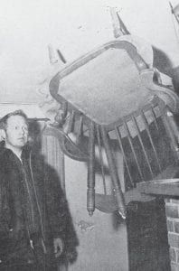 This upside-down chair is impaled in the ceiling of the Steve Quaife home, which was ruined by an explosion in March 1971. The chair evidently took flight, turned upsidedown and pierced the ceiling. According to an account of the event in the March 18, 1971 News-Herald, an accumulation of gas was suspected as the cause of the blast, since there had been a smell of gas the past couple days. However, three checks by gas company men did not discover a leak. Fortunately, none of the family members were home at the time of the blast, which also broke out a large plate glass window, buckled a wall, blew the roof loose from the walls, and threw an end table out the window and into the snow in front of the house. The residence was part of Tomteboda, the cabin resort owned and operated by the Quaifes. Steve Quaife is shown here examining the aftermath of the explosion a week after it happened.