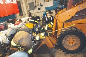 Firefighter I and II Instructor Terry Spieker of the Hovland Fire Department put these firefighter trainees through their paces in interior search and rescue training at a local garage. Firefighters’ masks were covered to simulate what it would be like to try to find a victim in dark and smoky conditions. Using an ax handle to feel their way through a maze of equipment, this crew successfully found someone needing rescue sitting in this bobcat.