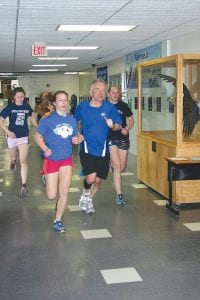 Although the CCHS track team has gotten outdoors to run a few times, much of their first month of training has been indoors at the school. Here Coach Chris Hegg, with Alyssa Martinson on his shoulder, follow Maya McHugh while just behind on the left Audrey Summers (wearing the volunteer T-shirt) works hard to keep up with the pace.