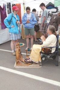 Kim Knutson multitasks, spinning and chatting with arts festival visitors.