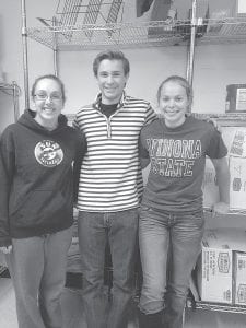 National Honor Society senior members Brenna Hay, Andrew Thompson, and Libby Zafft standing in front of empty shelves awaiting donations. Look for the NHS students on Halloween night.