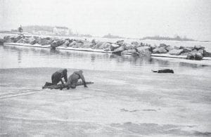 The annual Emergency Services Conference was held April 19 and 20, 1996 and featured a “rescue” as part of the cold-water rescue training. This archival photo shows two trainees venturing onto the thin ice of Grand Marais harbor to help a stricken victim. The rescue was successful.